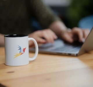 Image of a Zammad mug with a person working on a laptop in the background.